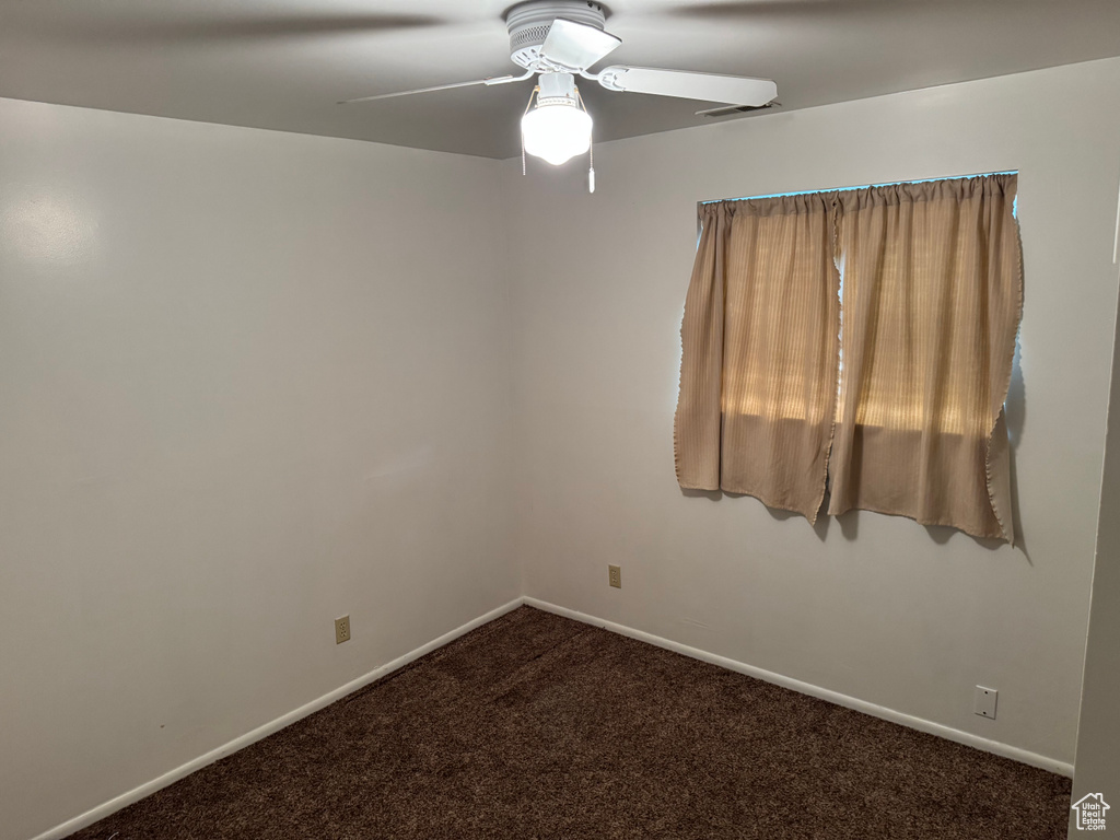 Unfurnished room featuring ceiling fan, dark carpet, and baseboards
