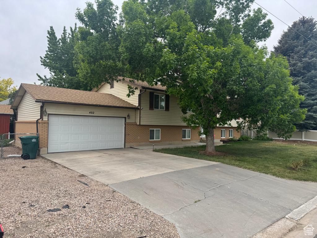 Split level home featuring brick siding, an attached garage, concrete driveway, and a front lawn
