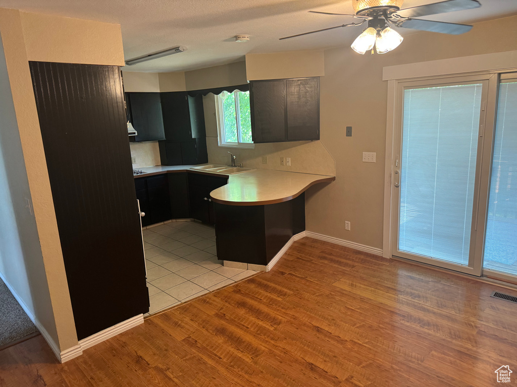 Kitchen featuring a peninsula, a ceiling fan, light countertops, light wood-type flooring, and a sink