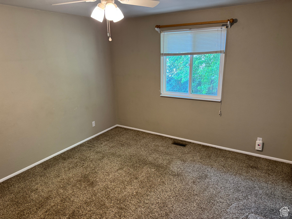 Carpeted spare room featuring ceiling fan and baseboards