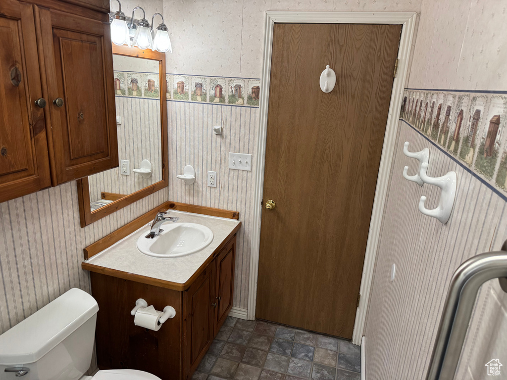 Bathroom with vanity, toilet, wallpapered walls, and stone finish flooring