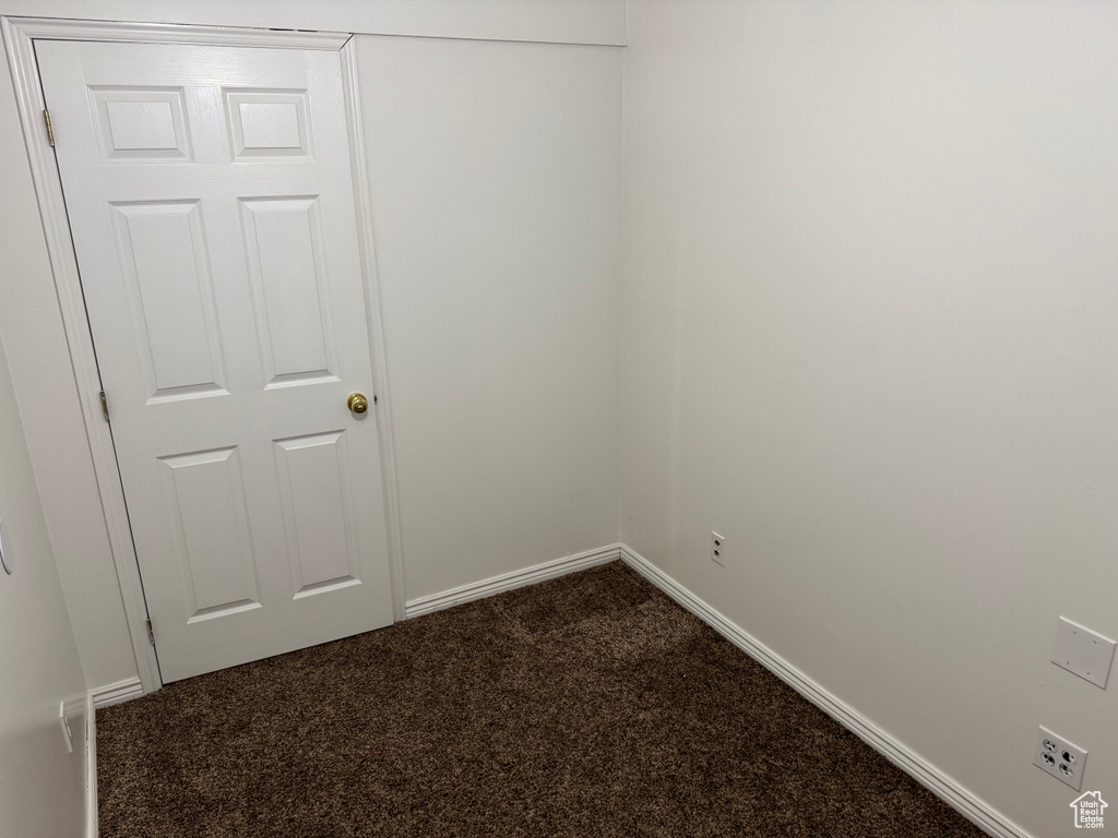 Unfurnished room featuring dark colored carpet and baseboards