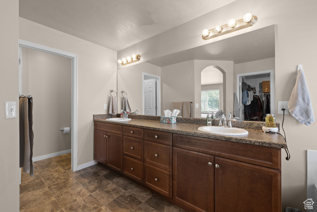 Full bath featuring double vanity, a walk in closet, baseboards, and stone finish floors