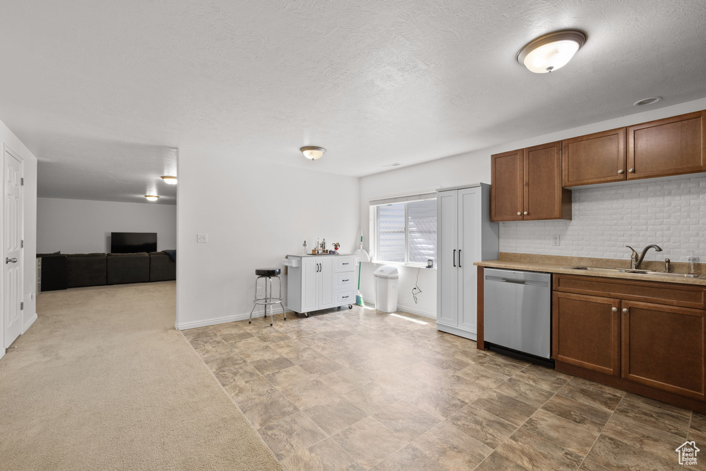 Kitchen with stainless steel dishwasher, a sink, decorative backsplash, brown cabinets, and light countertops
