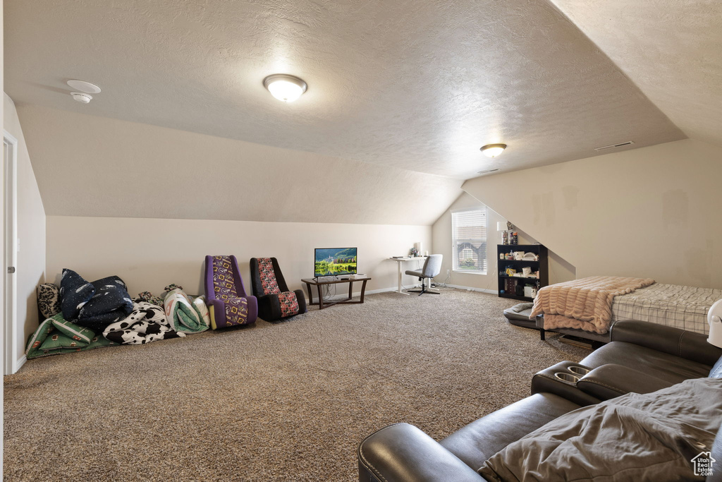 Interior space with a textured ceiling, carpet flooring, vaulted ceiling, and baseboards
