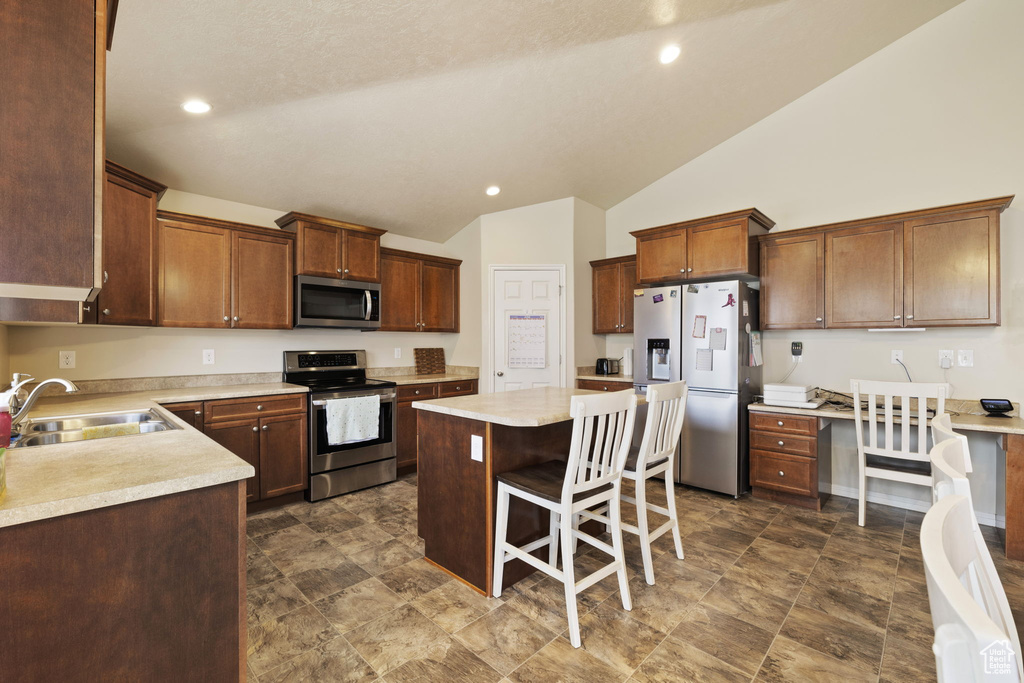 Kitchen with stainless steel appliances, a sink, lofted ceiling, a center island, and light countertops