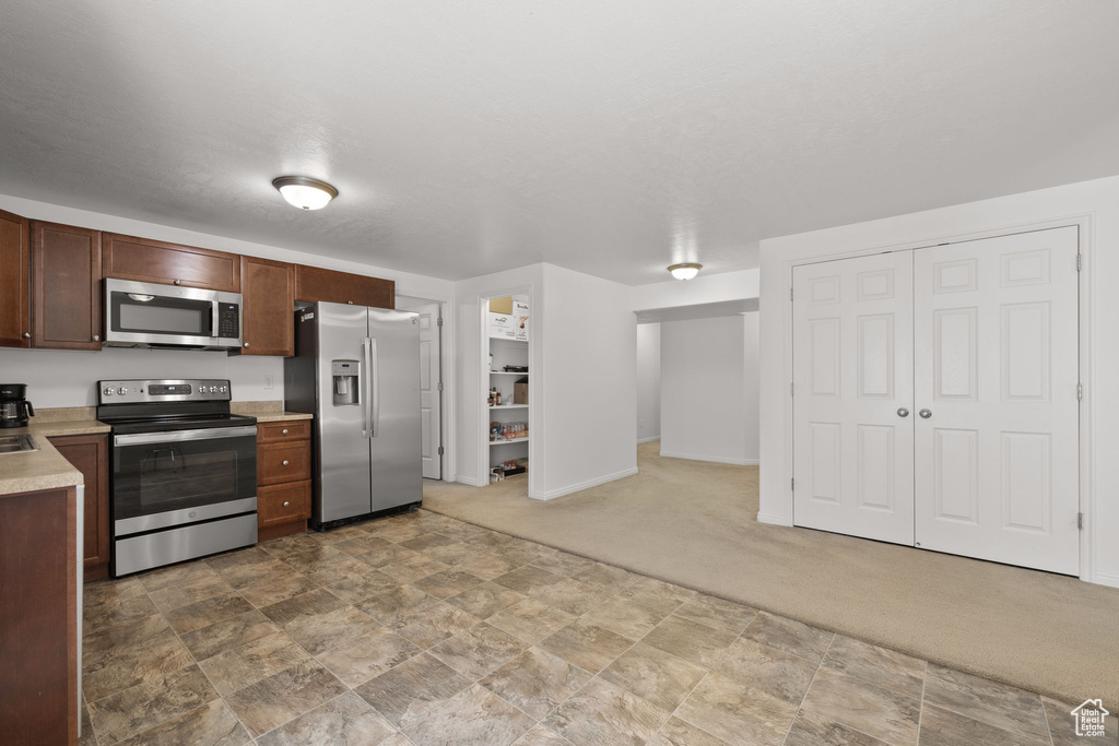 Kitchen with appliances with stainless steel finishes, light countertops, carpet, baseboards, and stone finish flooring