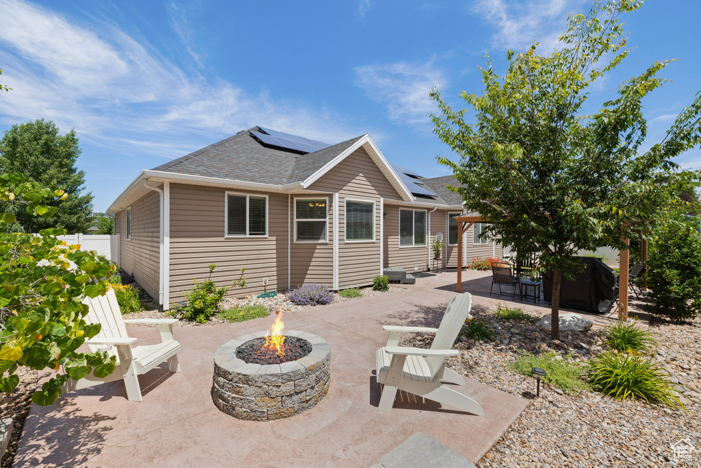 Back of house with an outdoor fire pit, a patio area, roof with shingles, and solar panels