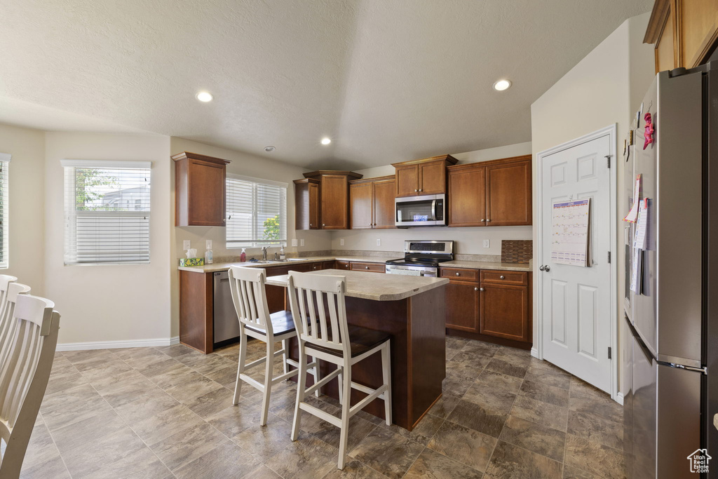Kitchen featuring appliances with stainless steel finishes, light countertops, brown cabinets, a kitchen island, and recessed lighting