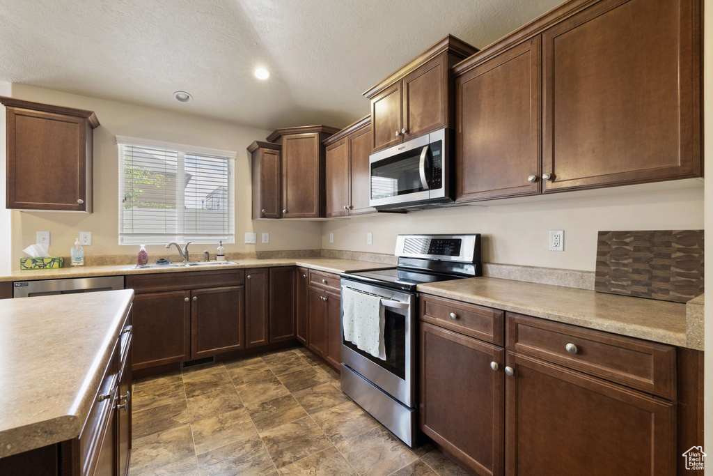 Kitchen featuring stainless steel appliances, a sink, light countertops, stone finish floors, and recessed lighting