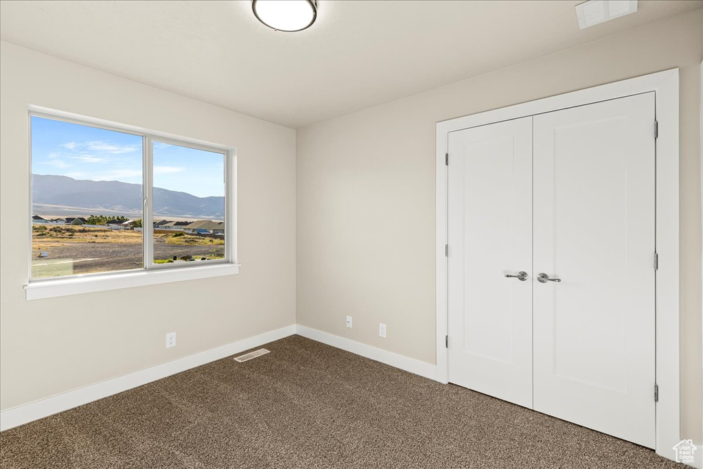 Unfurnished bedroom featuring dark carpet, a mountain view, baseboards, and a closet