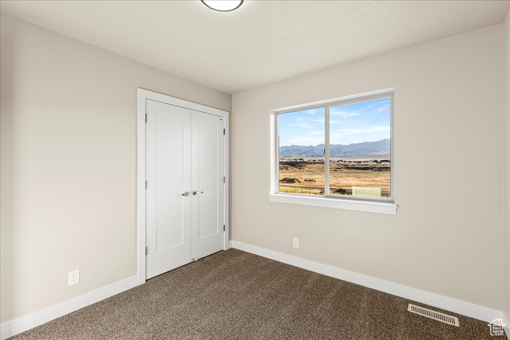 Unfurnished bedroom with dark carpet, baseboards, a mountain view, and a closet