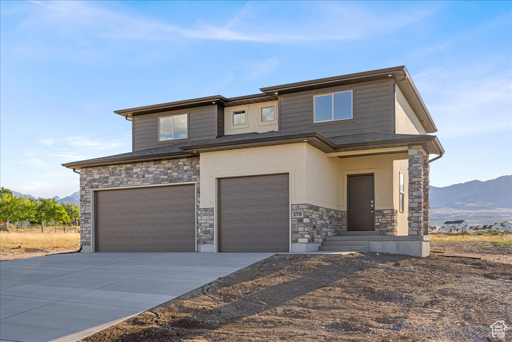 View of front of house with stone siding, an attached garage, a mountain view, and concrete driveway