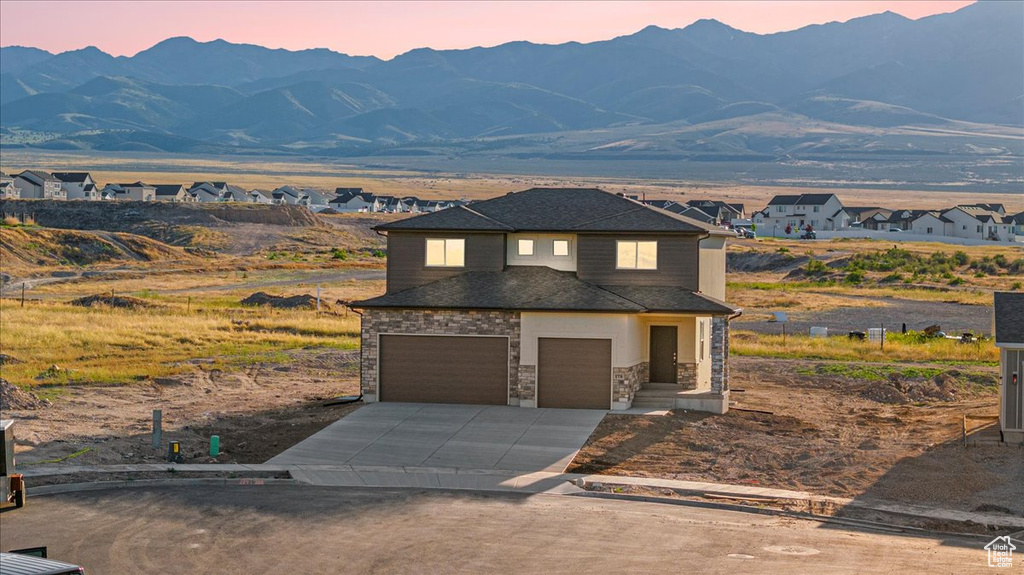 View of front of property with a garage, concrete driveway, stone siding, and a mountain view