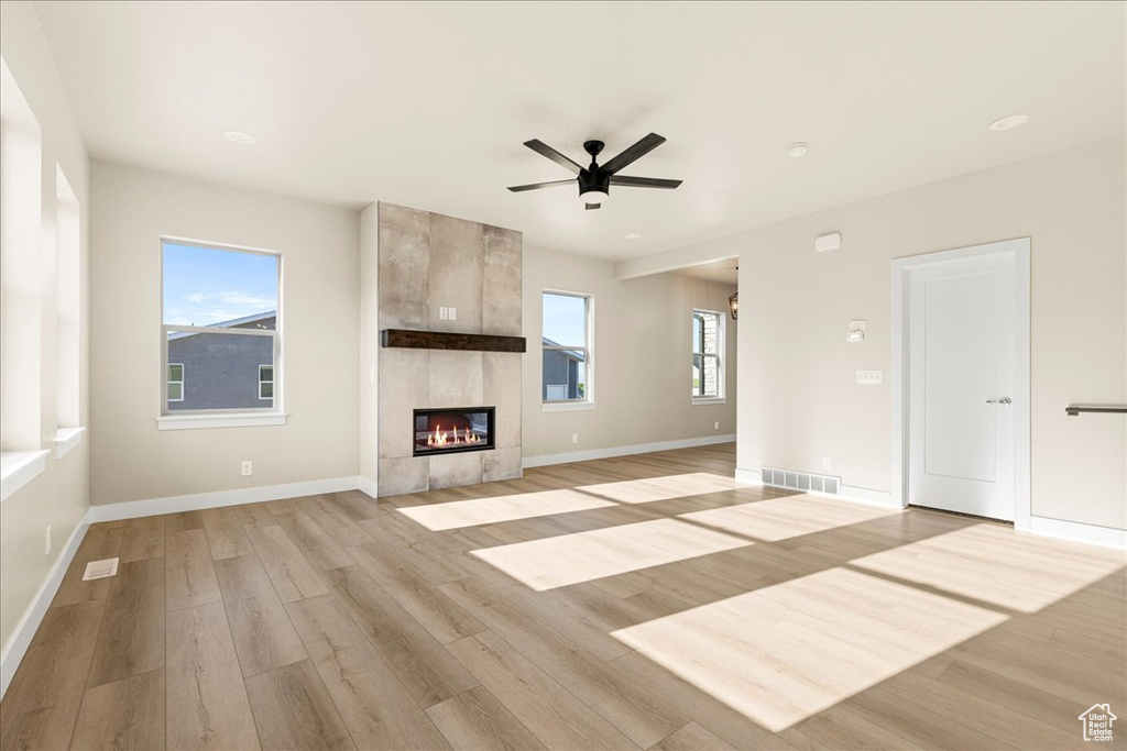 Unfurnished living room with light wood-type flooring, ceiling fan, baseboards, and a tiled fireplace