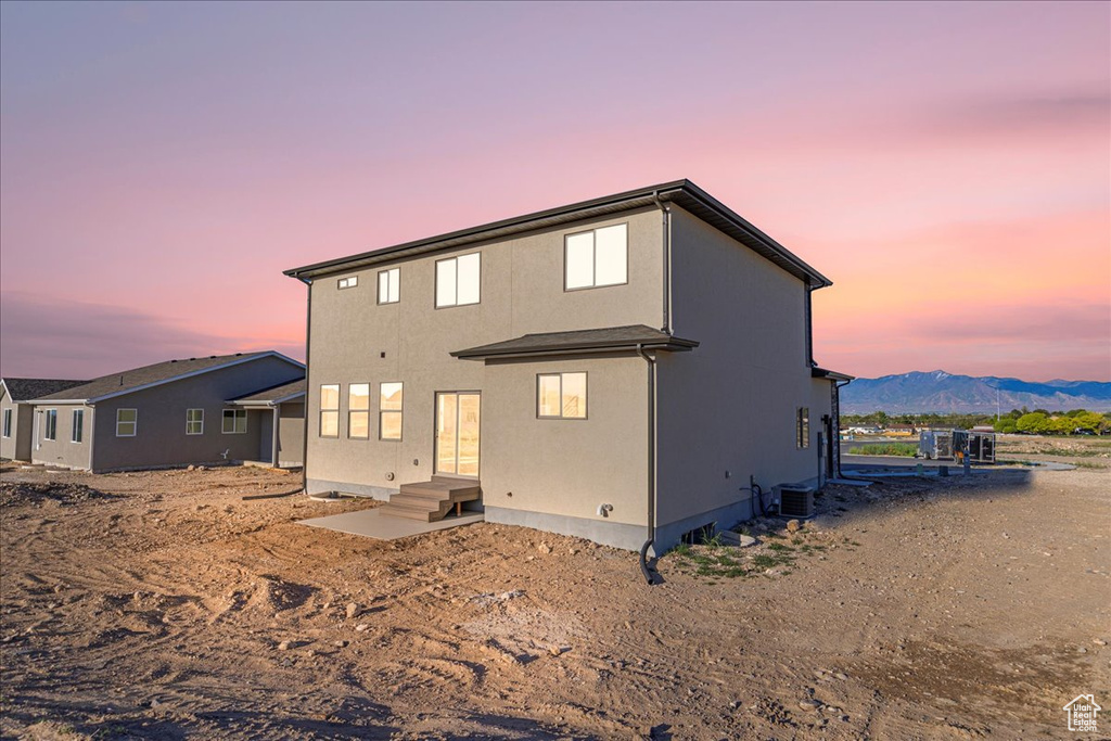 Back of property at dusk featuring cooling unit, a mountain view, and stucco siding