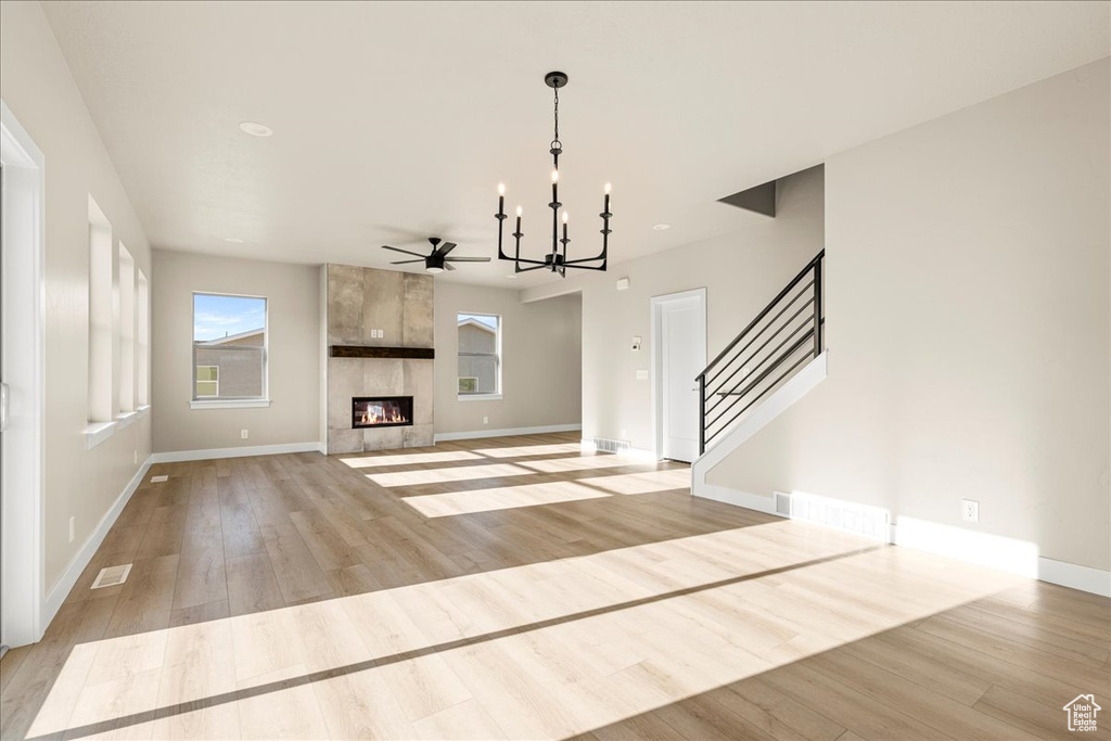 Unfurnished living room with a chandelier, light wood-style floors, baseboards, stairway, and a fireplace