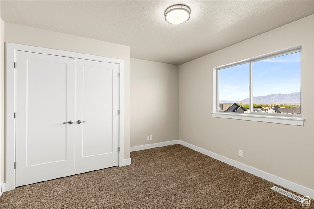 Unfurnished bedroom with baseboards, carpet flooring, a closet, a mountain view, and a textured ceiling