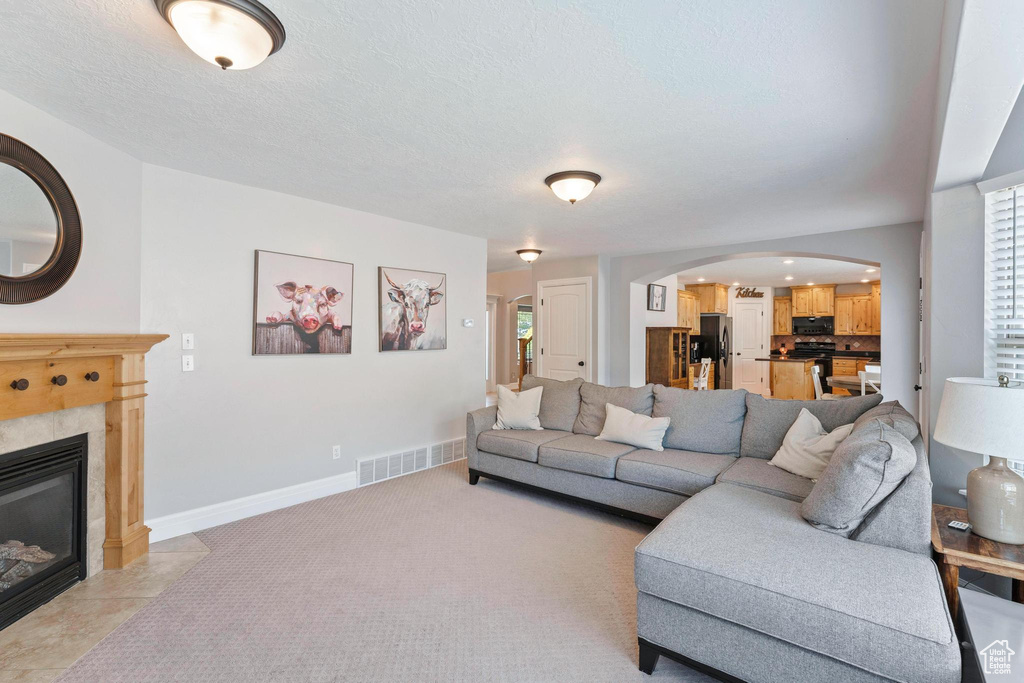 Living room featuring arched walkways, a tiled fireplace, baseboards, and plenty of natural light
