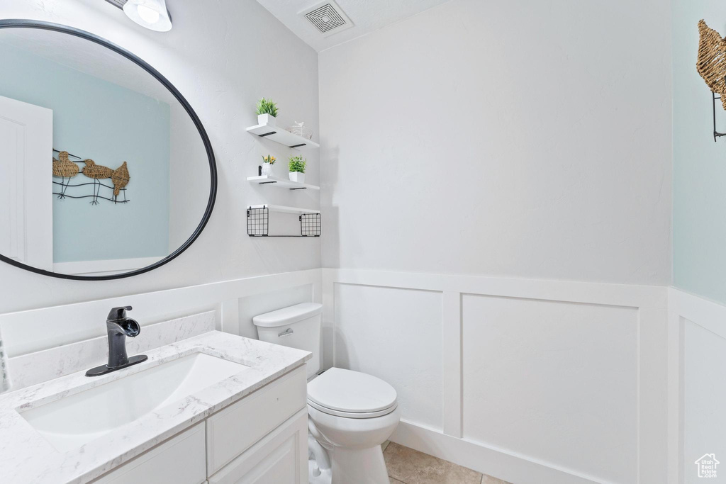 Half bath with a wainscoted wall, vanity, toilet, a decorative wall, and tile patterned flooring