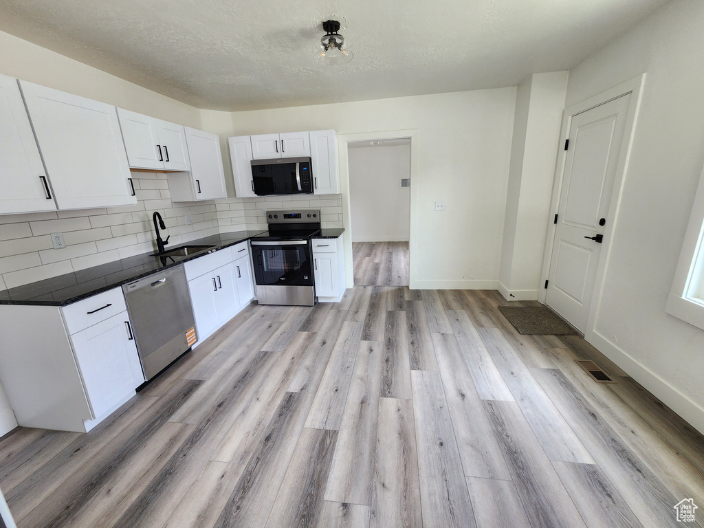 Kitchen featuring stainless steel appliances, a sink, dark countertops, white cabinetry, and backsplash