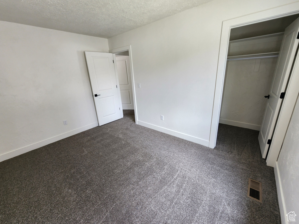 Unfurnished bedroom featuring dark colored carpet, a textured ceiling, baseboards, a closet, and a walk in closet