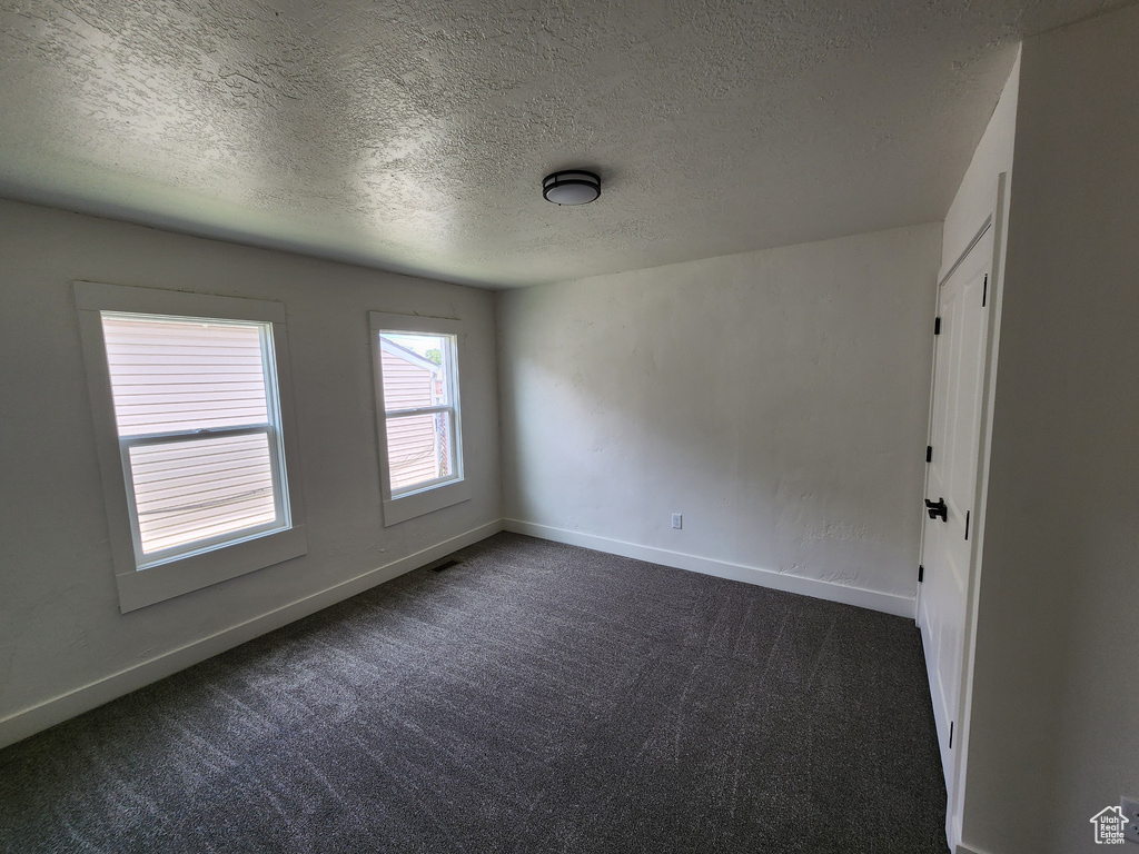 Unfurnished room with dark carpet, a textured ceiling, and baseboards