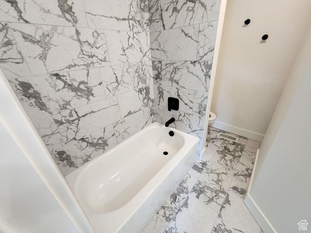 Bathroom featuring toilet, marble finish flooring, baseboards, and  shower combination