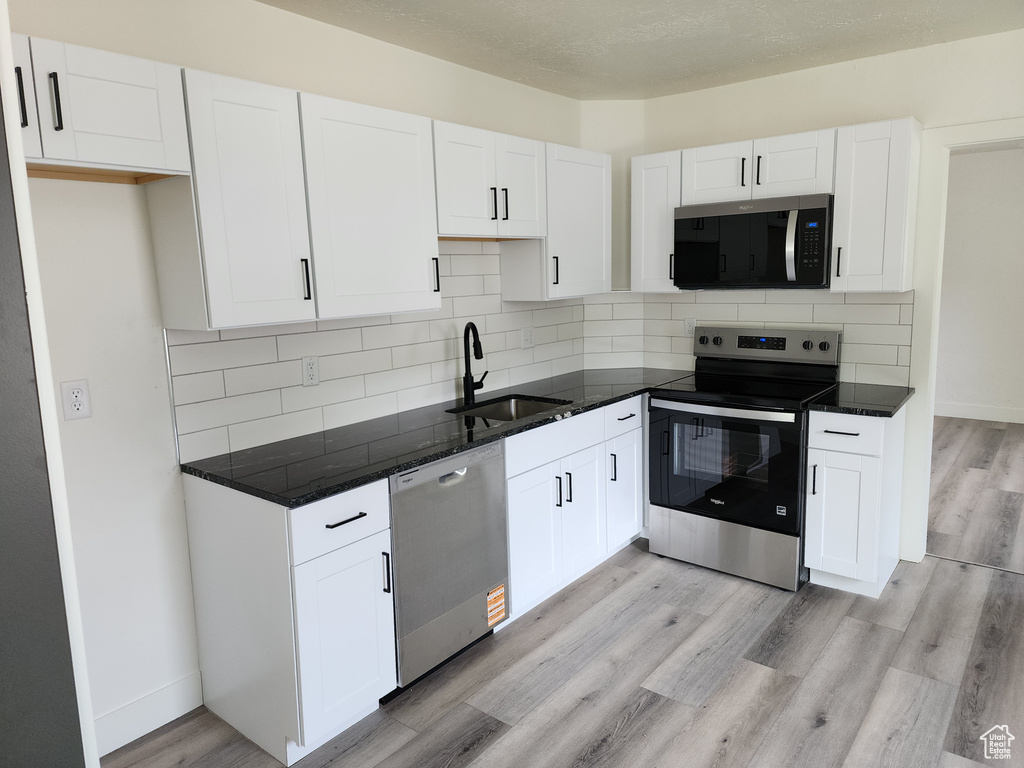 Kitchen featuring appliances with stainless steel finishes, a sink, white cabinetry, light wood-style flooring, and backsplash