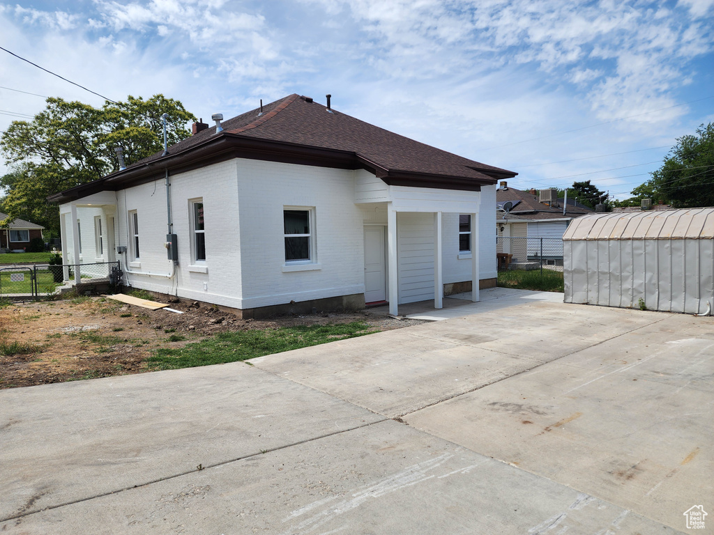 Back of property featuring a shingled roof, brick siding, and an outbuilding