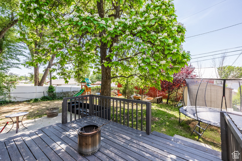 Wooden deck featuring an outdoor fire pit, a playground, a trampoline, and a fenced backyard