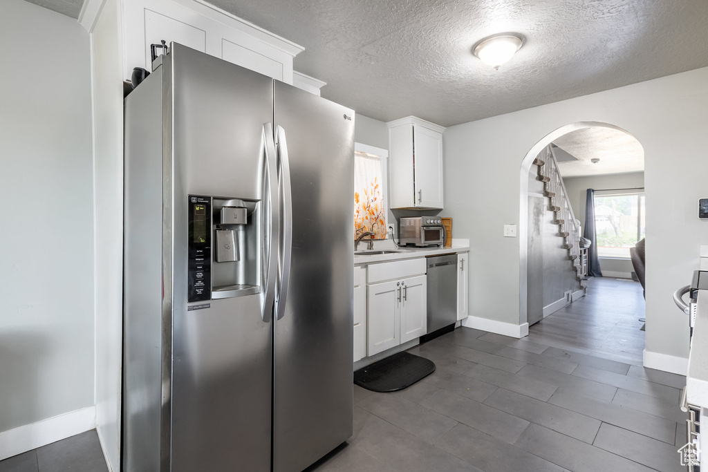 Kitchen with appliances with stainless steel finishes, arched walkways, a sink, baseboards, and a textured ceiling