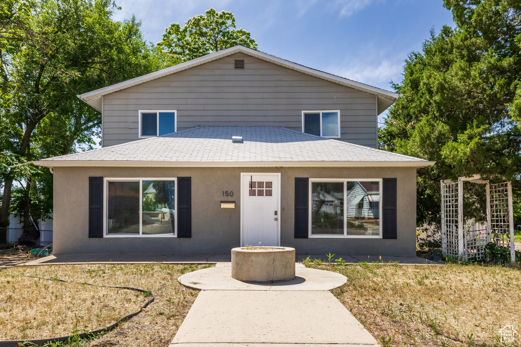 View of front facade with stucco siding, a shingled roof, a patio area, and a front lawn