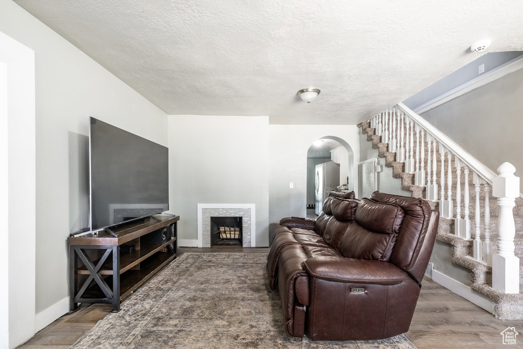 Living room featuring arched walkways, stairs, a textured ceiling, wood finished floors, and baseboards