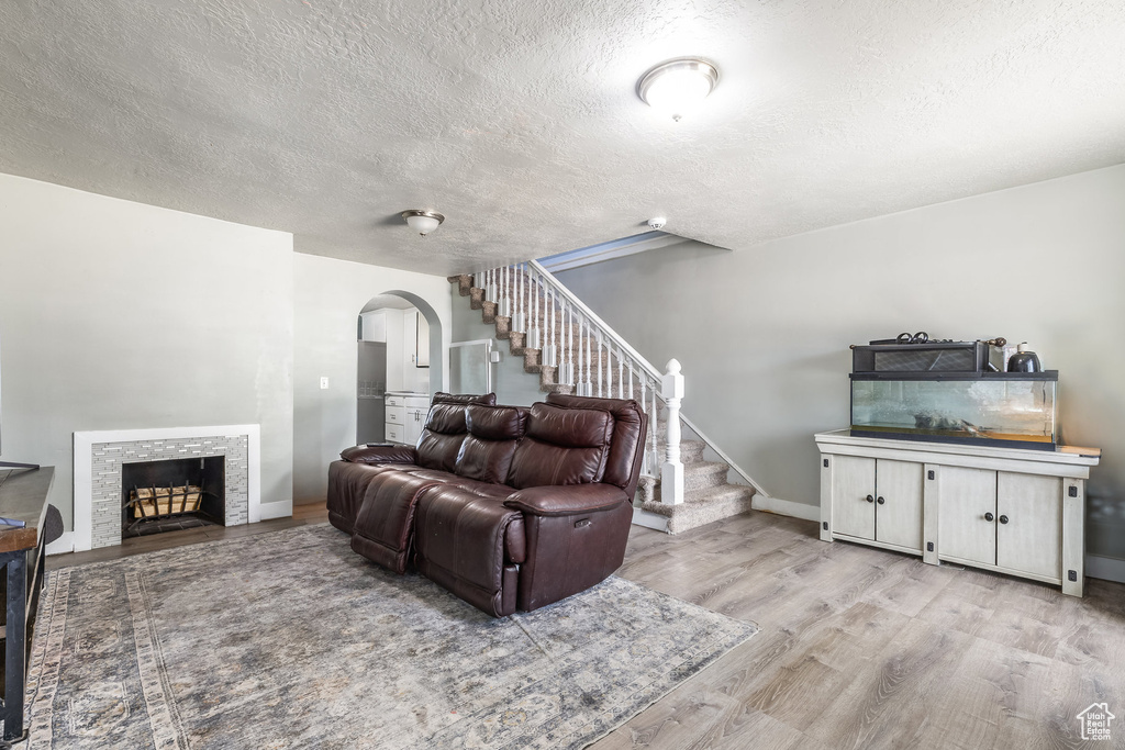 Living area featuring arched walkways, a textured ceiling, stairs, light wood-style flooring, and baseboards