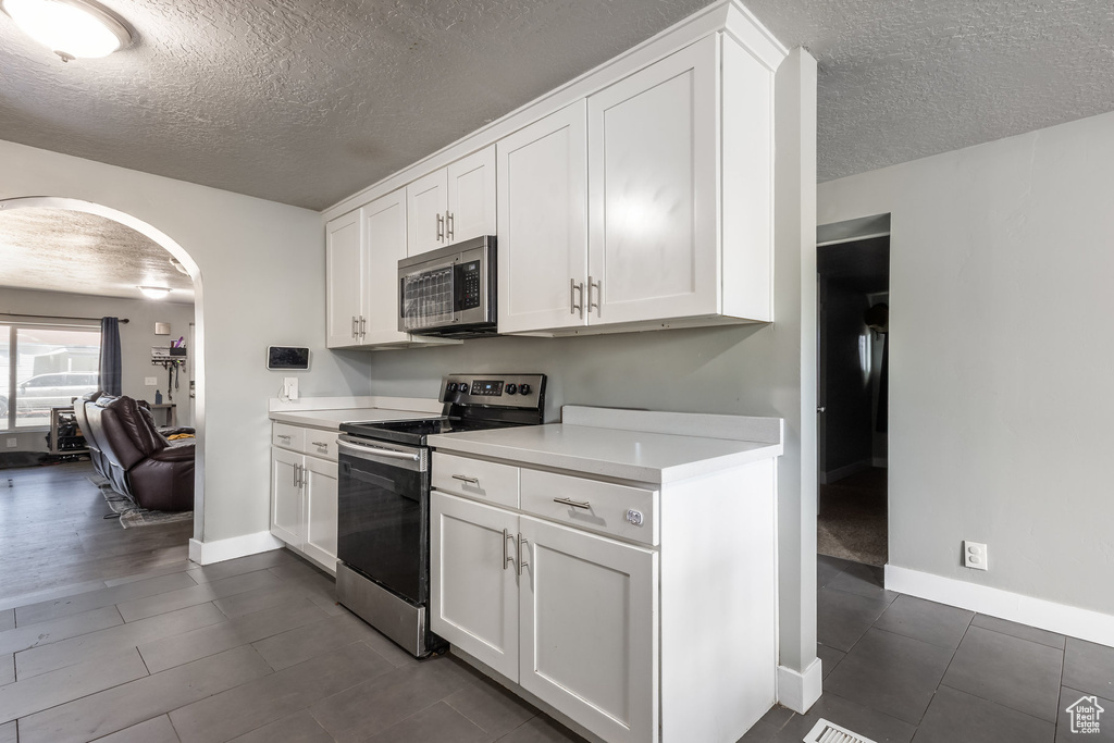 Kitchen with appliances with stainless steel finishes, arched walkways, a textured ceiling, light countertops, and white cabinetry