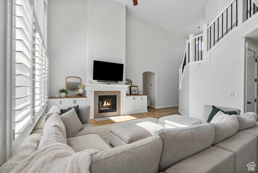 Living room featuring a towering ceiling, plenty of natural light, light wood-type flooring, a fireplace with flush hearth, and baseboards