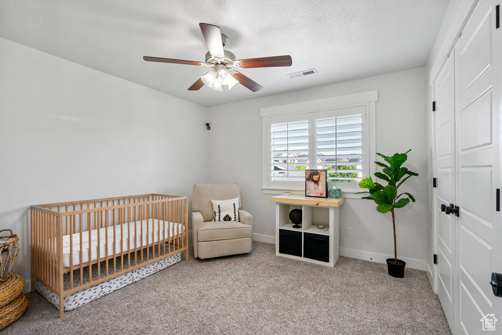 Carpeted bedroom with a nursery area, baseboards, and a ceiling fan