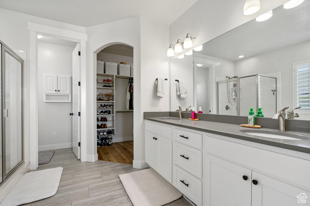 Full bath with a stall shower, double vanity, a walk in closet, baseboards, and recessed lighting
