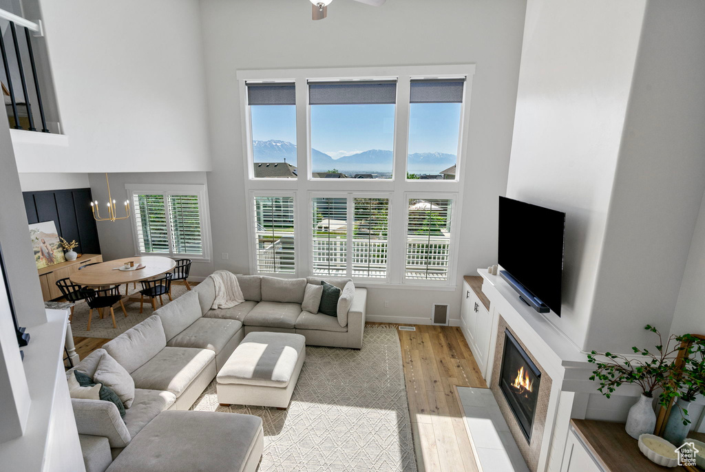 Living room with light wood finished floors, a high ceiling, a fireplace with flush hearth, a chandelier, and baseboards