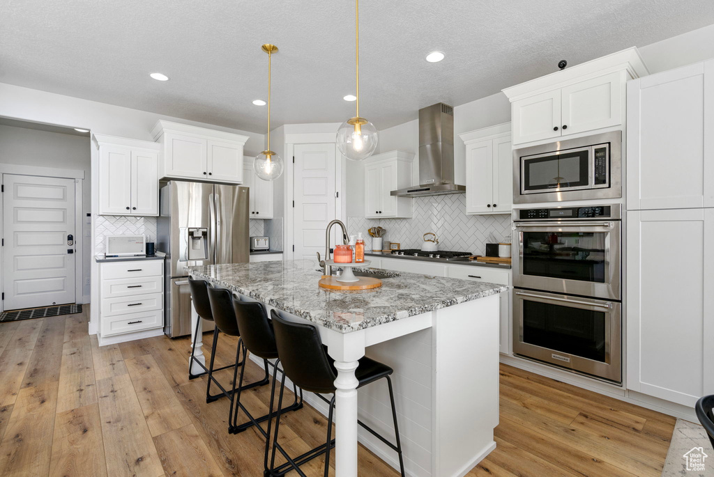 Kitchen featuring stainless steel appliances, wall chimney range hood, a sink, tasteful backsplash, and light wood-type flooring