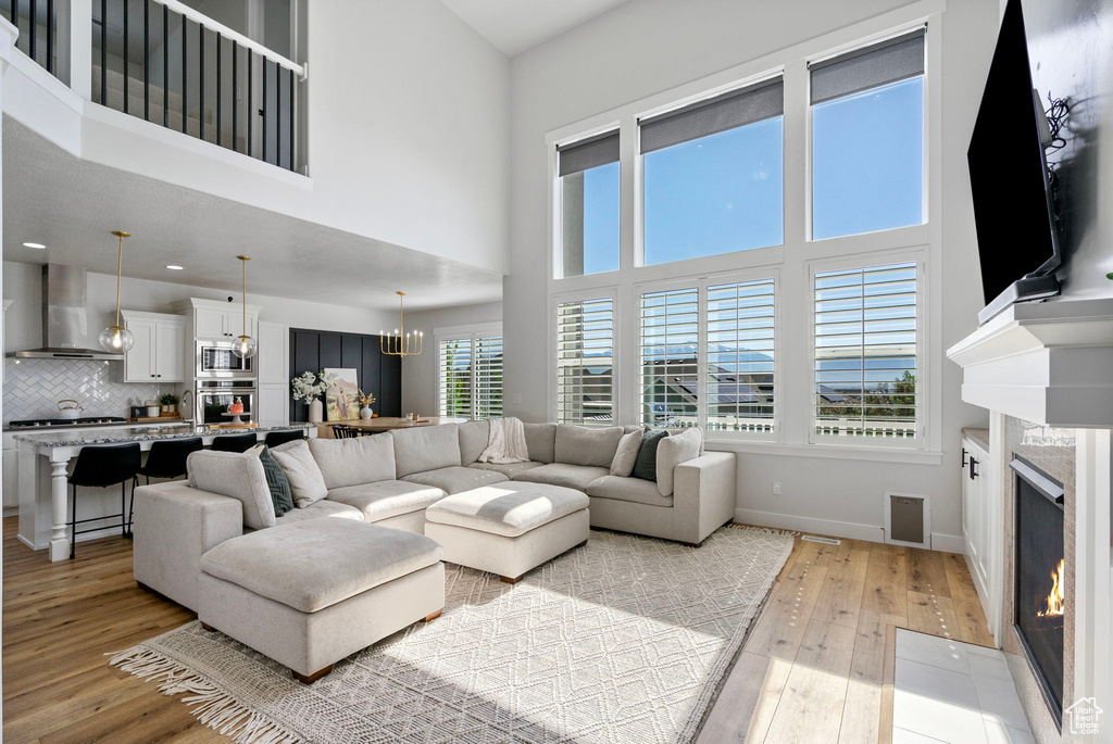 Living room featuring light wood finished floors, a high end fireplace, baseboards, a chandelier, and a towering ceiling