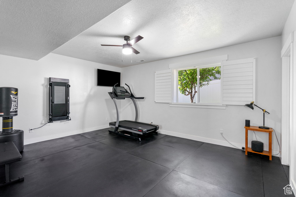Workout room featuring baseboards, a textured ceiling, and ceiling fan