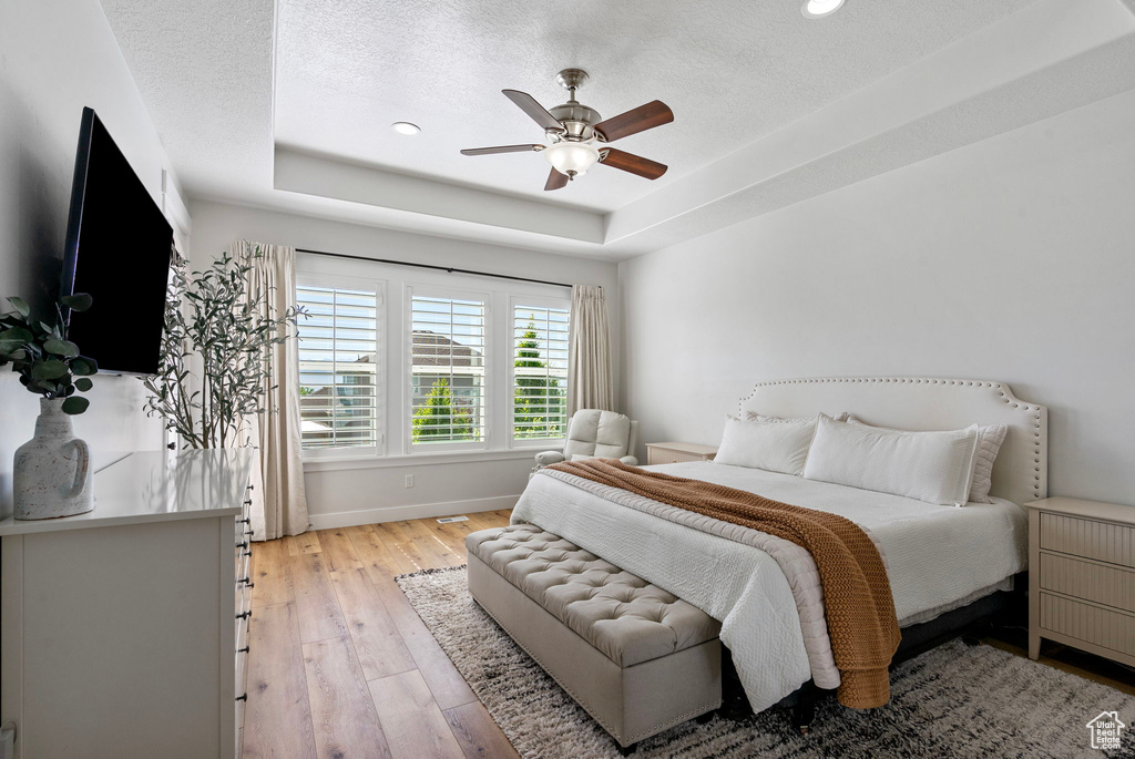 Bedroom featuring a raised ceiling, light wood-type flooring, baseboards, recessed lighting, and a textured ceiling