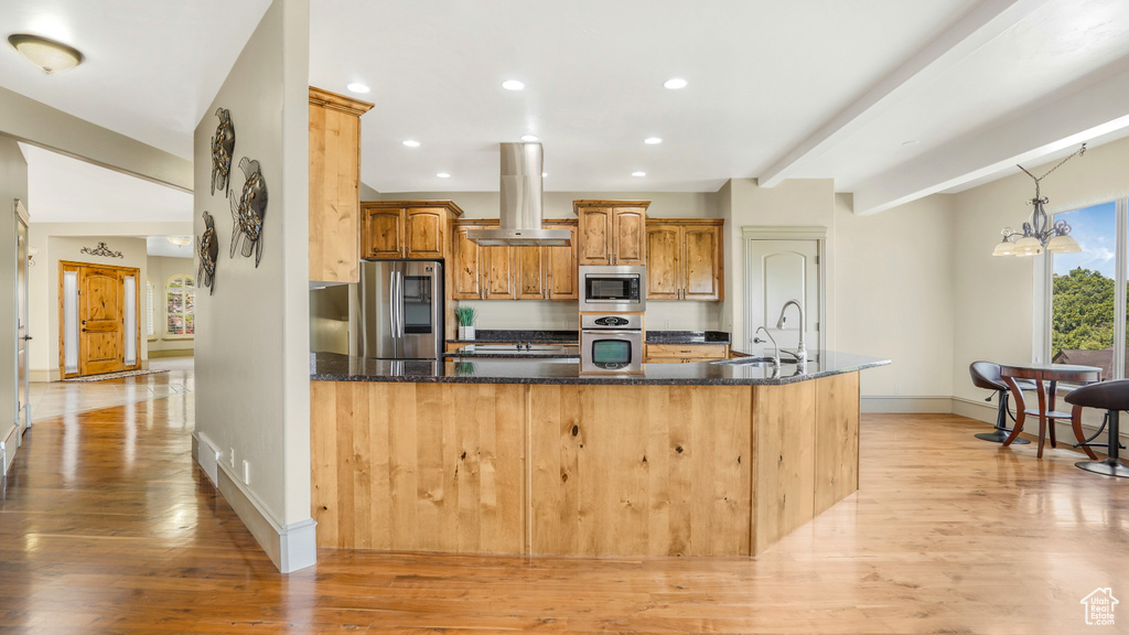 Kitchen with appliances with stainless steel finishes, island exhaust hood, light wood finished floors, baseboards, and recessed lighting
