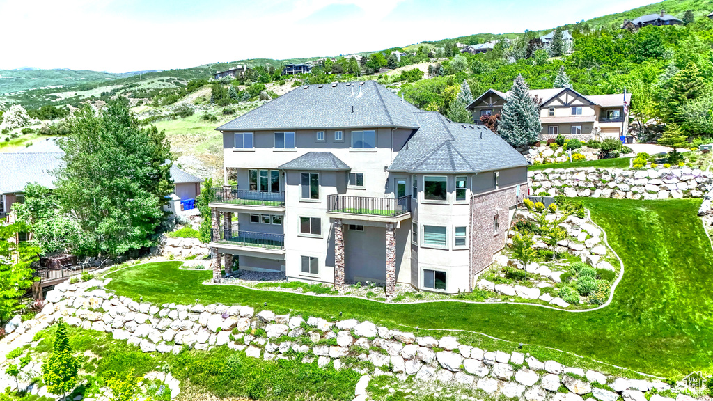 Rear view of property featuring a balcony, stucco siding, and stone siding
