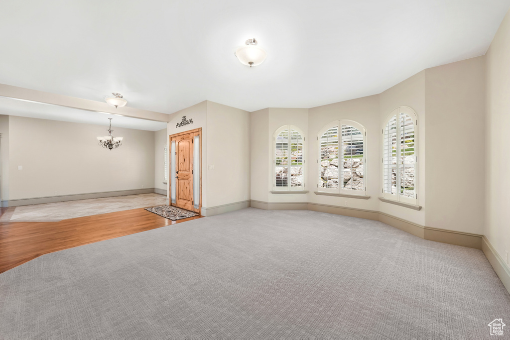 Spare room featuring light colored carpet, a chandelier, and baseboards