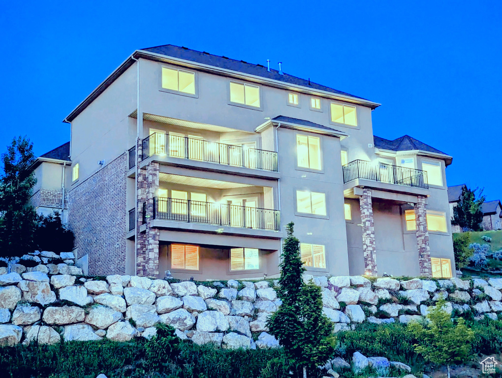 Rear view of house with stucco siding, a balcony, and stone siding