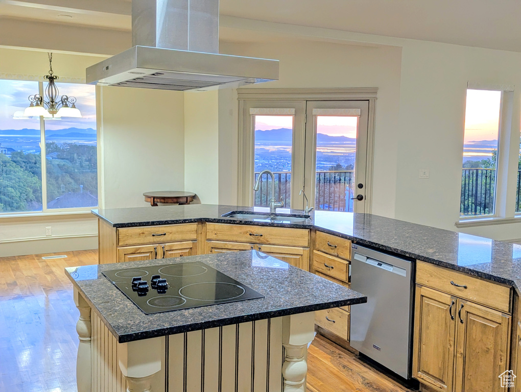 Kitchen featuring wall chimney range hood, black electric cooktop, dishwasher, a sink, and light wood finished floors