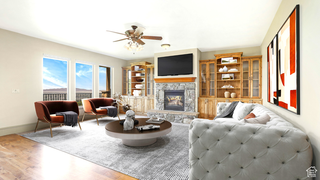 Living area with wood finished floors, a ceiling fan, a stone fireplace, and baseboards